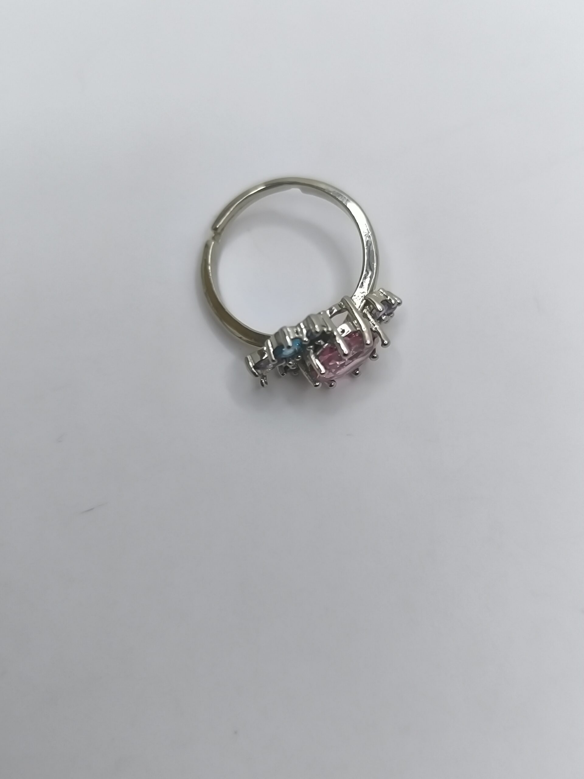 نمای نزدیک از انگشتر طرح گل با نگین صورتی و نگینهای آبی و بنفش روی زمینه سفید.